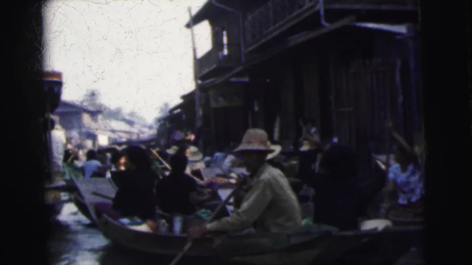 1962 Calcutta canal scene with a broad-hatted boatman, seated passengers, and dark wooden waterside architecture.
