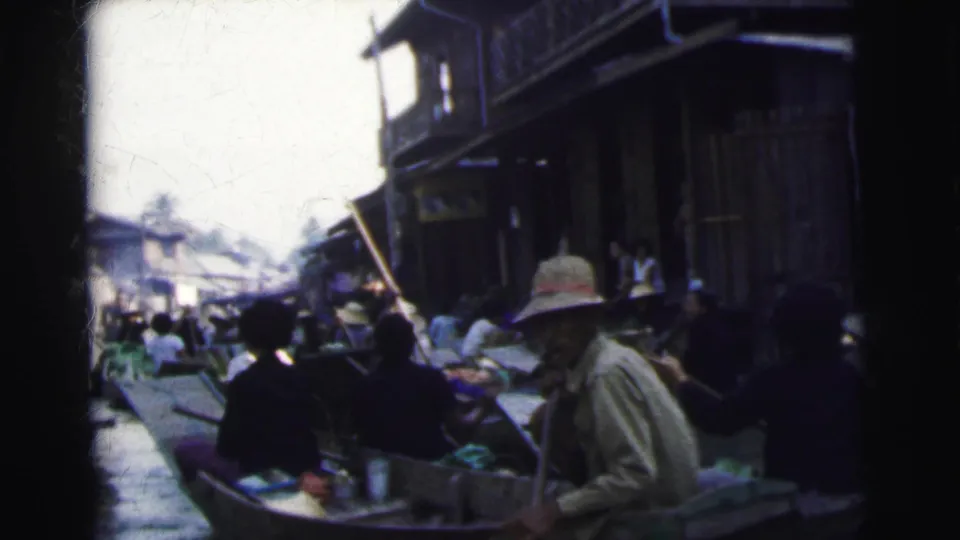 1962 Calcutta home-movie frame showing clustered boats, seated passengers, a boatman, and canal-side wooden buildings.