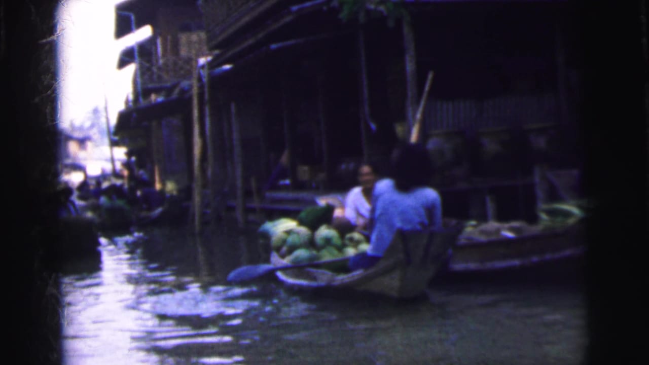 A produce-laden boat passes close to riverside buildings in the 1962 Calcutta floating market scene.