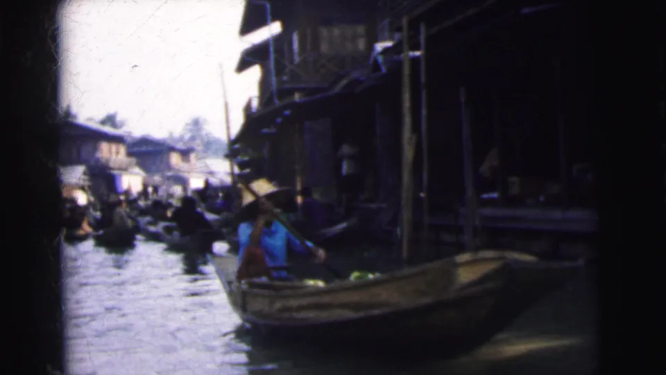 A paddled wooden boat moves through the Calcutta floating market waterway with more boats visible beyond.