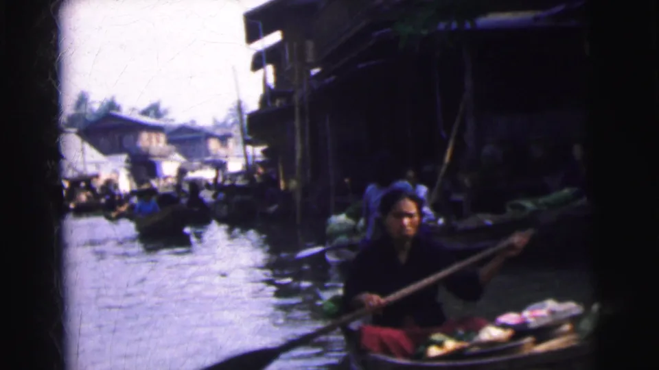 1962 Calcutta home-movie frame showing a person rowing a small boat through a crowded waterway market.