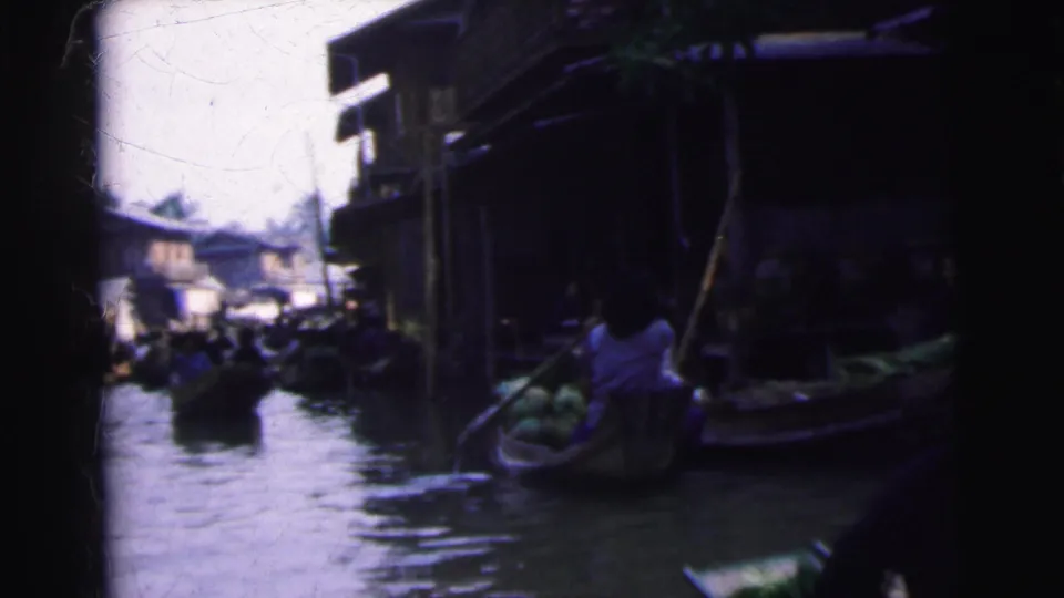 1962 Calcutta frame showing a produce boat near a dark waterside structure with busy canal traffic beyond.