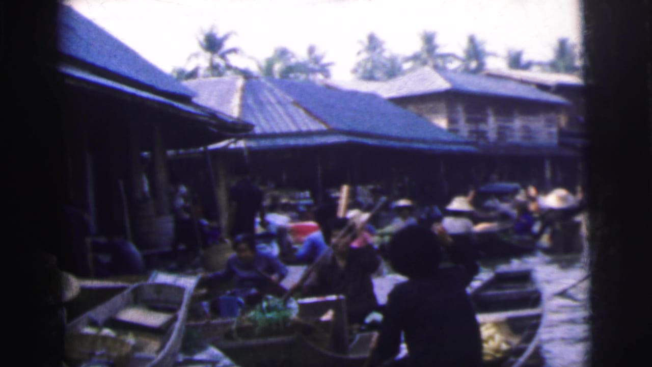1962 8mm frame of a crowded Calcutta waterway where people in small boats move through a market area lined with buildings.