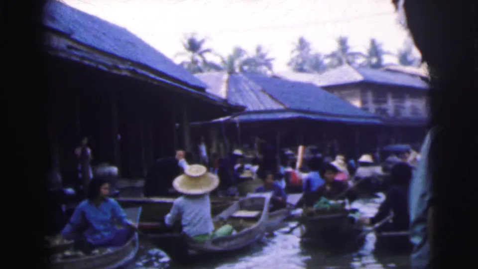 1962 Calcutta 8mm frame showing several small boats with people and produce beside roofed waterfront buildings.