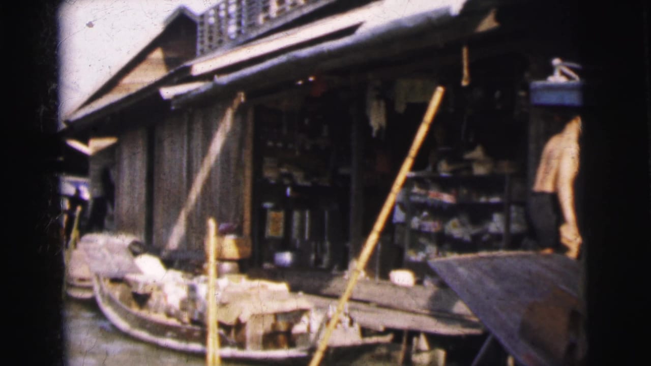 1962 Calcutta canal scene with a wooden boat, open shopfront, poles, and a person working at the waterline.