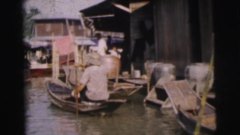 1962 Calcutta canal scene showing a seated paddler, moored wooden boats, shopfronts, and buildings close to the water.