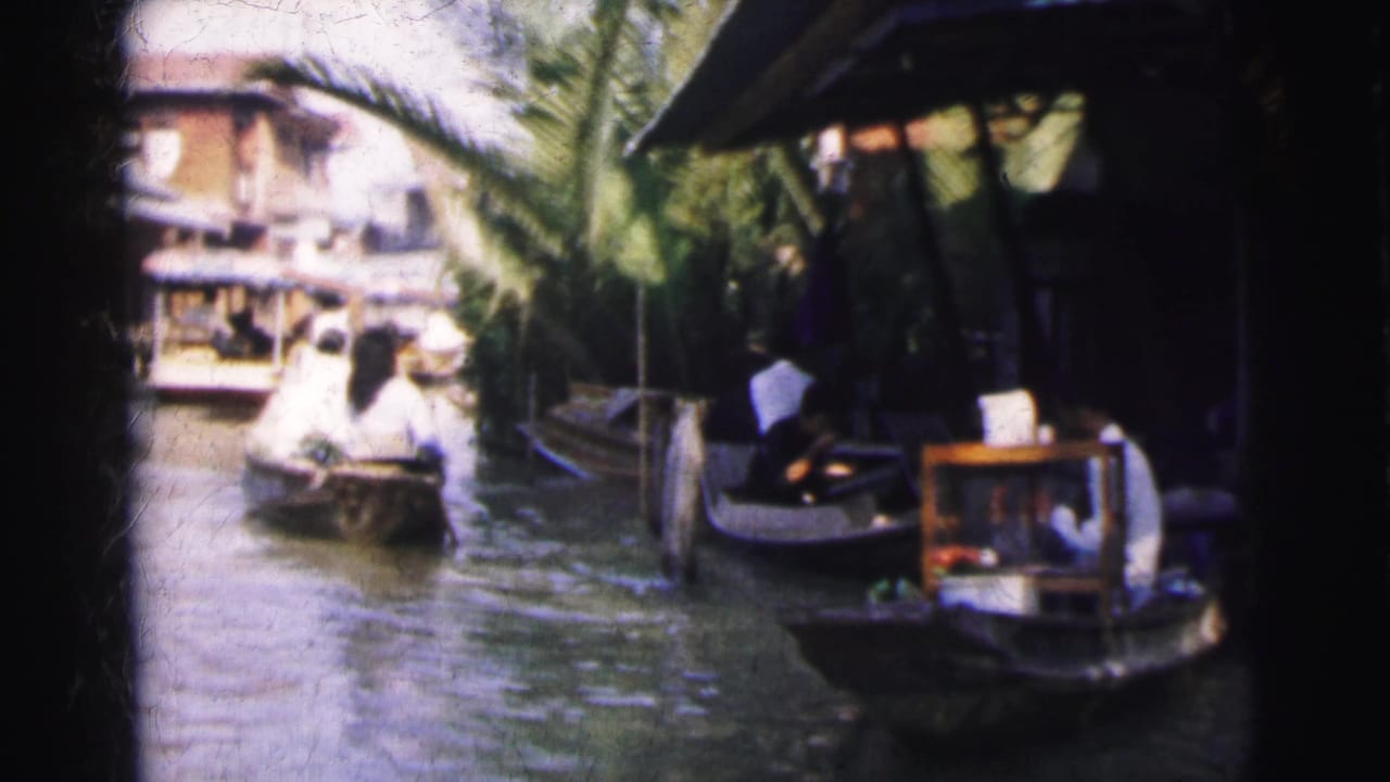 1962 Calcutta canal scene with small boats near wooden waterside structures and palm trees, filmed from a moving home-movie viewpoint.