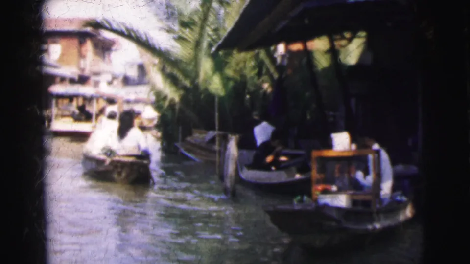 1962 Calcutta canal scene with small boats near wooden waterside structures and palm trees, filmed from a moving home-movie viewpoint.
