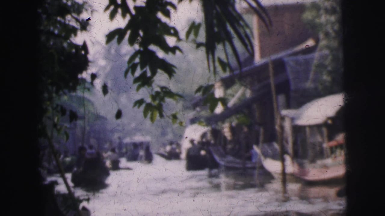 1962 Calcutta 8mm frame showing a river channel through leaves, with small boats and waterfront buildings in soft focus.