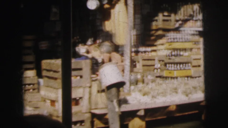 1962 Calcutta market view with stacked crates, rows of bottles, and ceramic vessels in soft 8mm color.