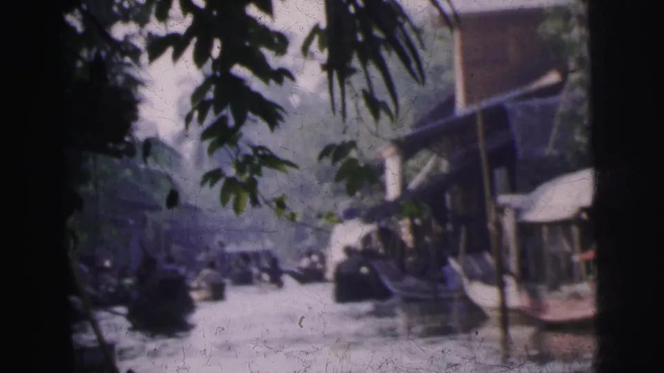 1962 Calcutta waterway view with small boats, leafy branches, a streetfront awning, and distant people near the bank.
