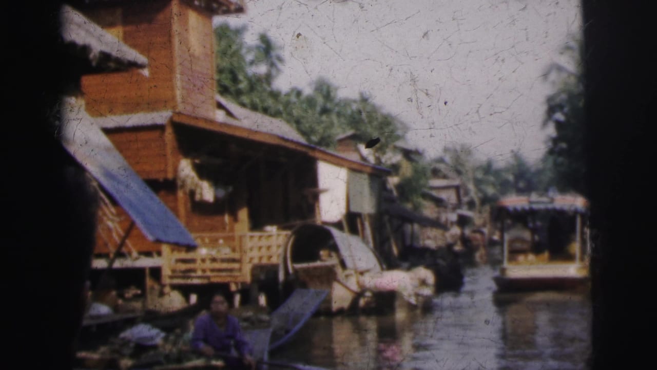 1962 Calcutta home-movie frame showing a canal lined with wooden structures and small boats, with a person near the water.
