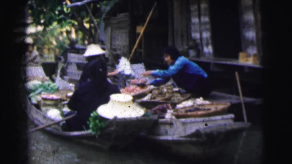 1962 Calcutta frame of vendors in boats handling produce beside a canal-side building, with woven hats visible.