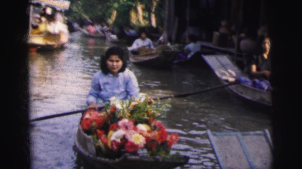 In 1962 Calcutta home-movie footage, a woman paddles a flower-laden boat through a busy canal with other boats nearby.