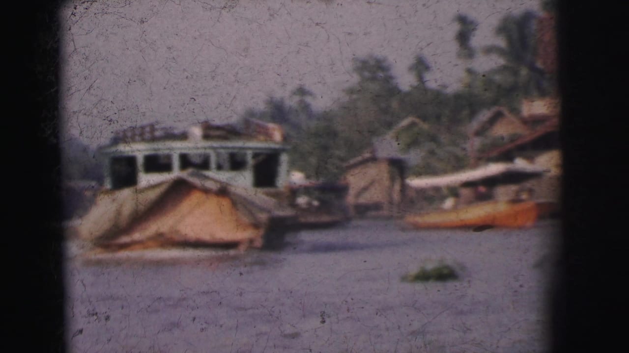 1962 Calcutta home-movie frame showing a covered boat or houseboat near wooden waterside structures and trees.