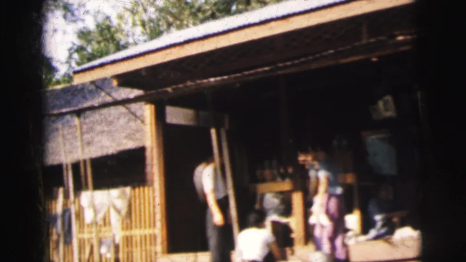 1962 Calcutta 8mm frame showing adults beside a doorway at a simple wooden waterside structure.