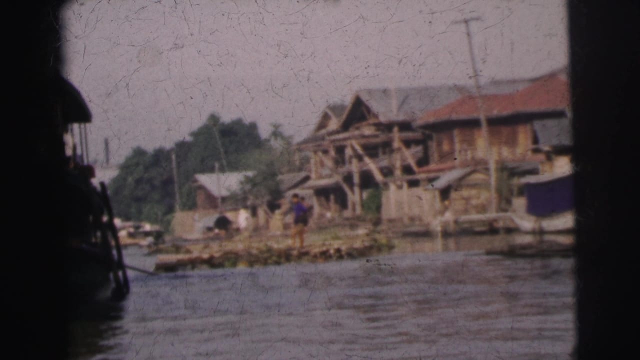 Riverside wooden structures and a dark boat silhouette seen from the water.