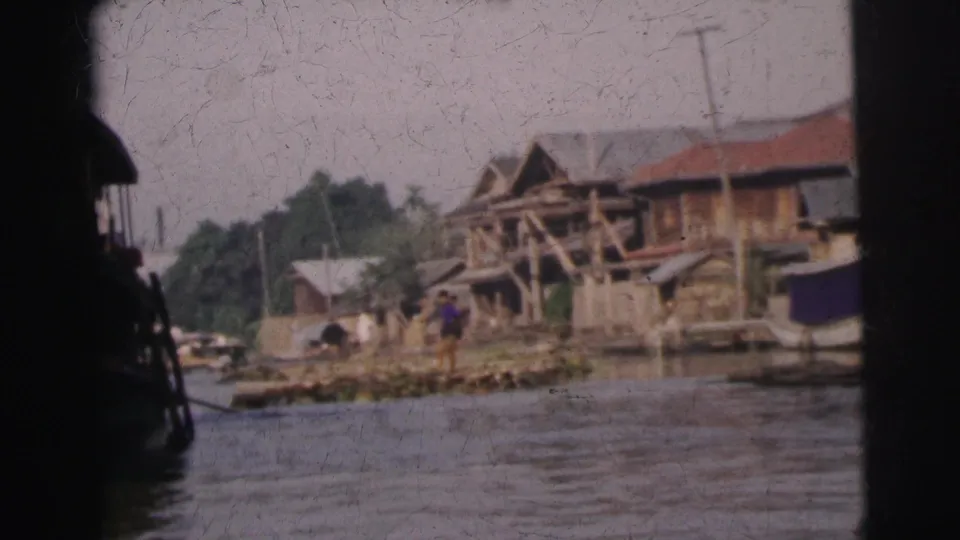 1962 Calcutta riverbank view with wooden huts, simple structures, and a dark passing boat shape in the foreground.
