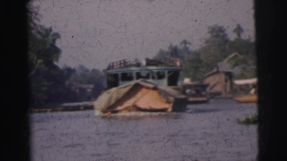 1962 Calcutta river scene with a covered small boat in the foreground and ferryboat traffic near riverside huts.