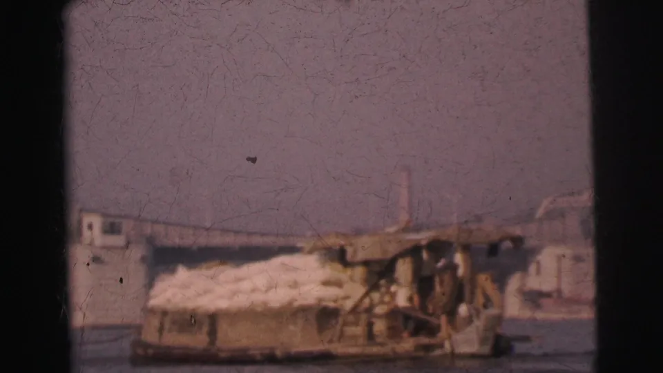 1962 Calcutta home-movie frame showing a loaded river barge with sacks and a bridge beyond the water.