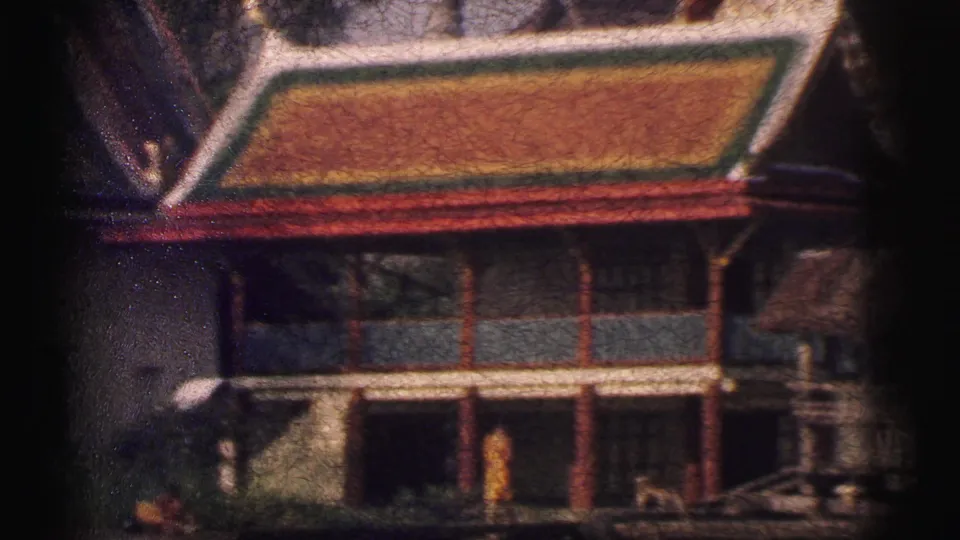 1962 travel footage frame showing a temple-like building with a colorful roof and a saffron-robed monk near the lower facade.
