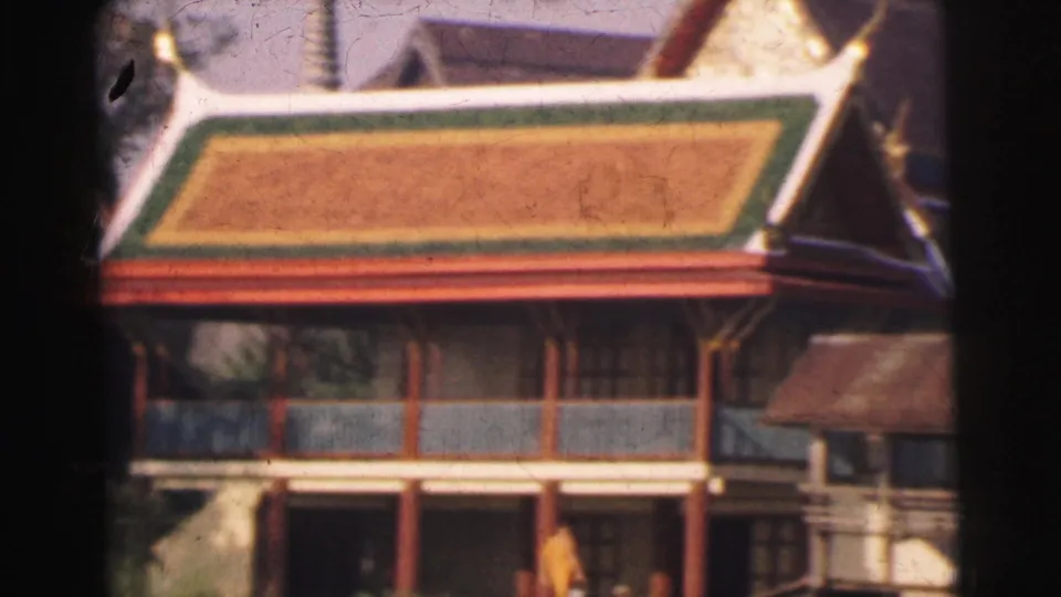 1962 home-movie frame with a closer view of a temple-like building, showing its colorful roof, balcony railings, and columns.