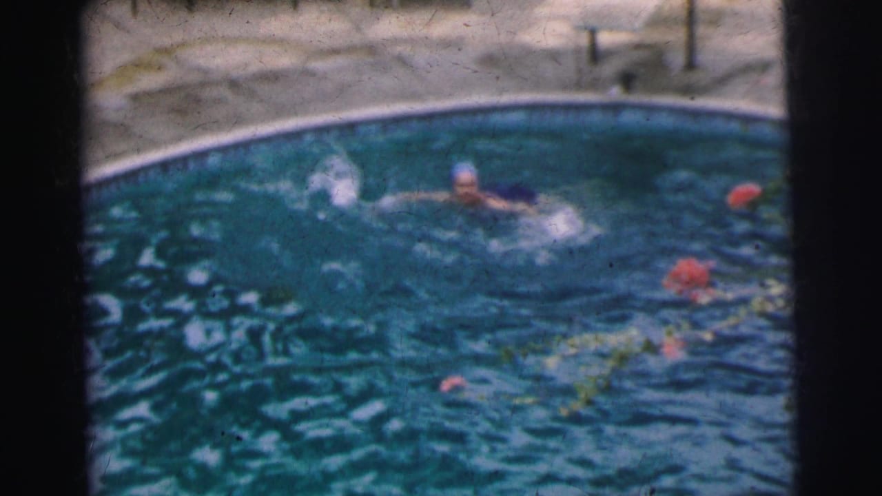 In 1962 Calcutta home-movie footage, a woman in a bathing cap swims crawl stroke through a curved backyard-style pool.