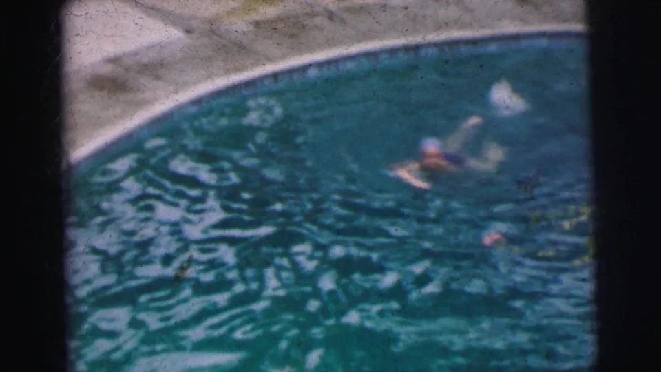 A home-movie frame shows the woman mid-lap in a 1962 Calcutta swimming pool, with grain and color fading visible.