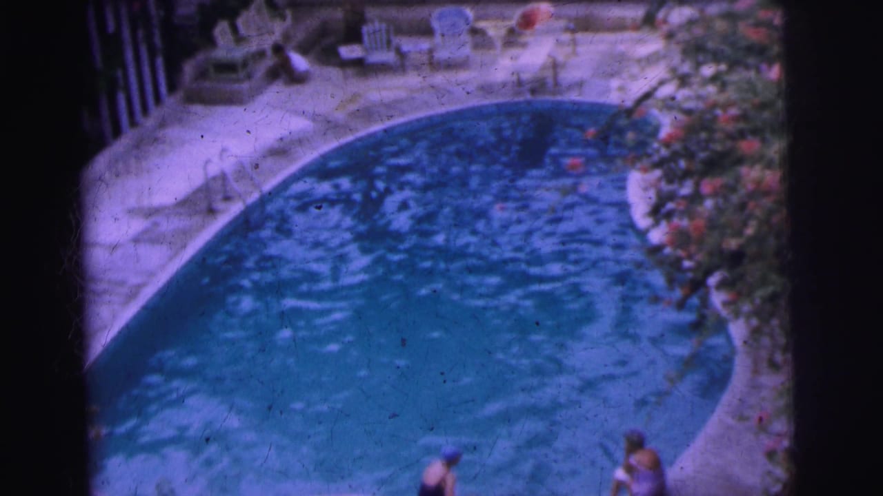 1962 Calcutta pool scene with rippling water, swimmers by the edge, white patio chairs, and garden planting.