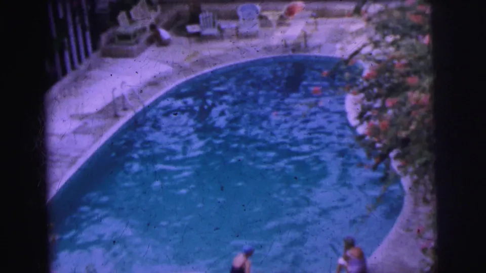 1962 Calcutta pool scene with rippling water, swimmers by the edge, white patio chairs, and garden planting.