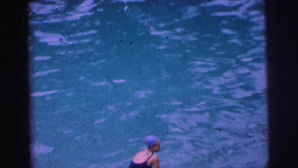 1962 Calcutta poolside frame with a woman in a blue swim cap and dark bathing suit partly visible against rippling water.
