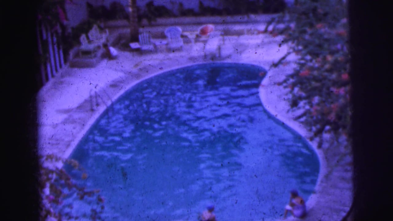 Curved swimming pool with lounge chairs and people near the deck.