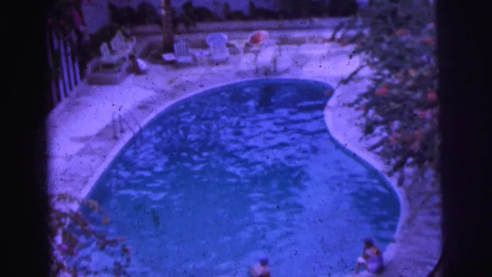 1962 Calcutta 8mm frame showing a kidney-shaped pool, pale deck, lounge chairs and people at the pool edge.