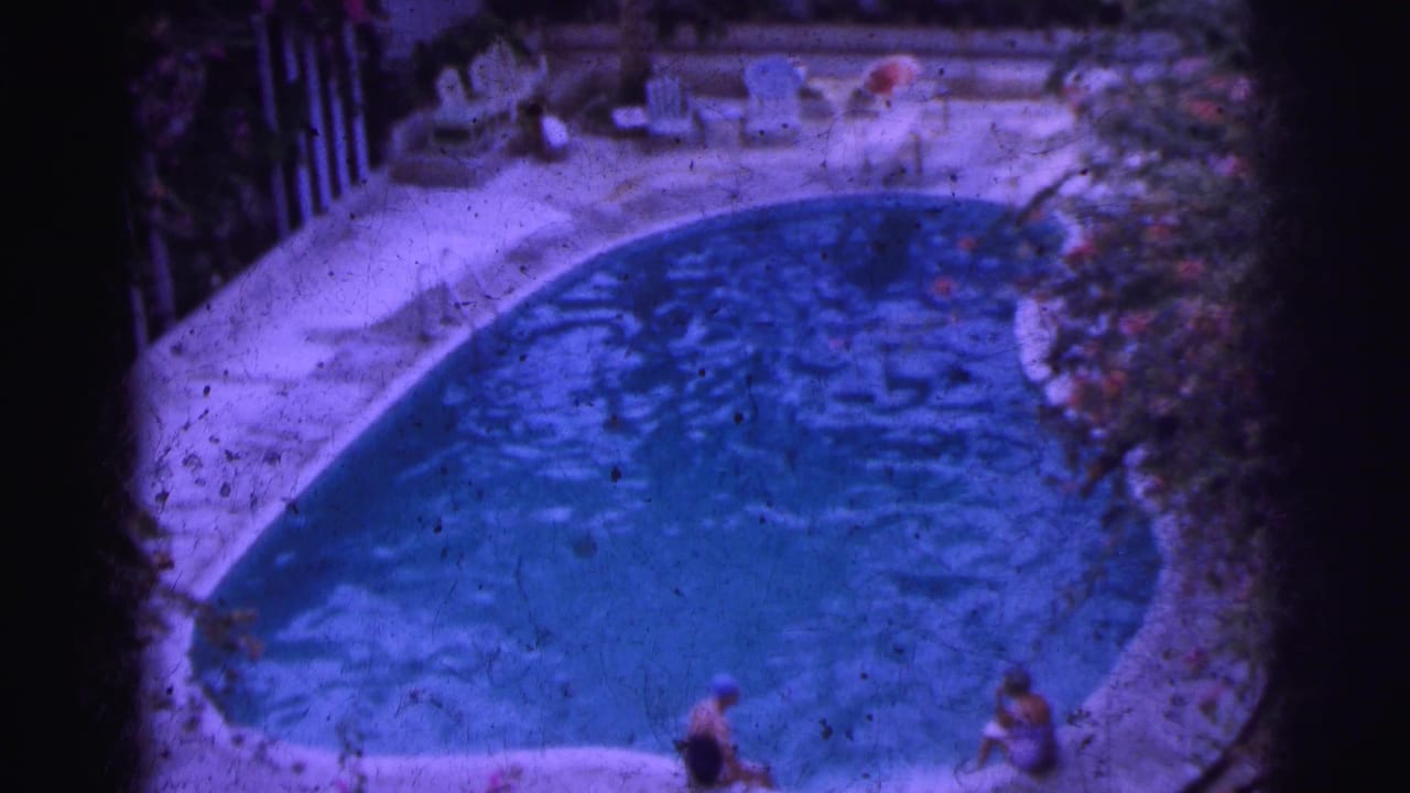 1962 Calcutta poolside frame with blue water, pale deck, lounge chairs and figures around the pool.