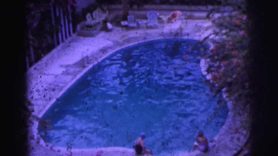 1962 Calcutta poolside frame with blue water, pale deck, lounge chairs and figures around the pool.