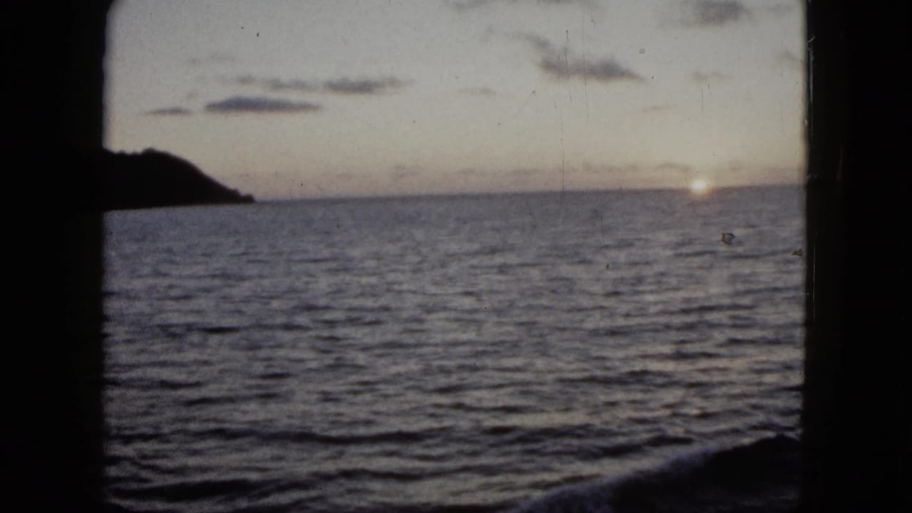 1962 Acapulco home-movie frame showing the sun near the ocean horizon with a dark coastal landform at left.
