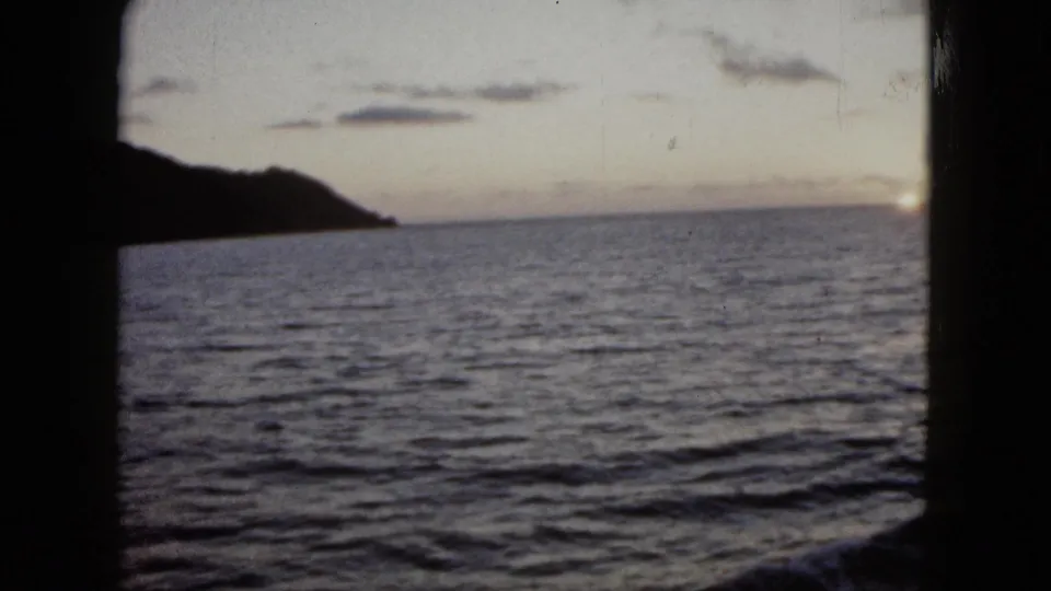 1962 Acapulco 8mm frame with open water, a silhouetted shoreline, and fading sky near sunset.