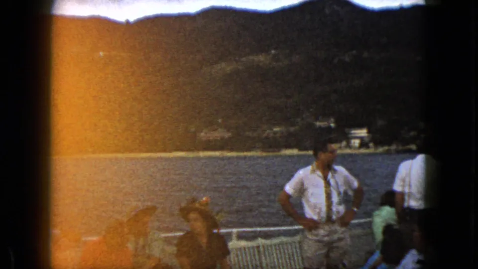 1962 Acapulco boat-deck view with adults in summer clothing near railings, backed by water and mountains.