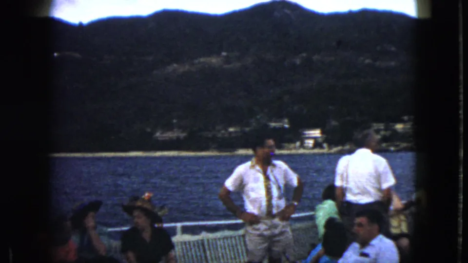 1962 Acapulco home-movie frame showing passengers gathered on deck with coastal mountains in the distance.