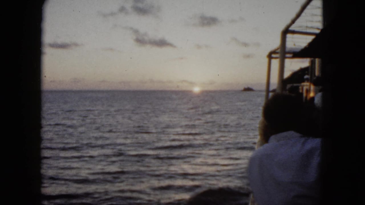 1962 Acapulco frame with rippled ocean, low sun near the horizon, a distant landform, and a man partly visible at the boat edge.