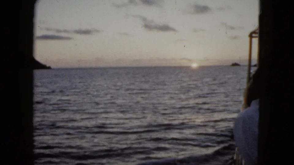 1962 Acapulco home-movie view across open water at sunrise, with distant landforms and the passenger partly obscured at the right edge.