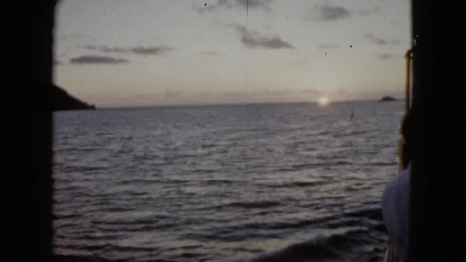 1962 Acapulco frame showing the ocean at sunrise from a boat, with a person cropped at the right edge and dark 8mm frame borders.