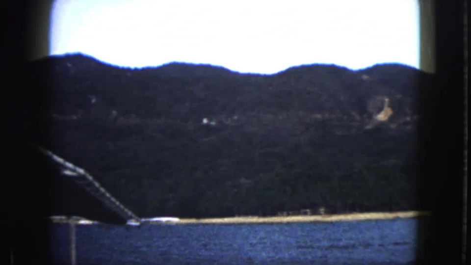 Acapulco boat-tour view focused on water, beach, wooded mountains, and a slanted piece of boat equipment at the edge.