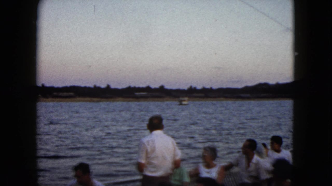 Boat passengers remain near the rail as water and a low shoreline fill the background.