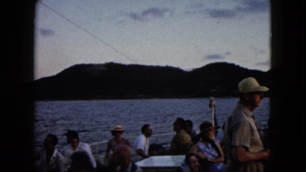 Passengers sit on a boat with water and dark hills behind them.