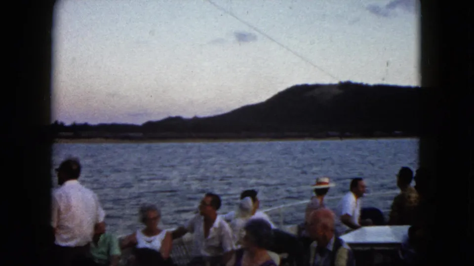 Adults aboard a boat in Acapulco, Mexico, including a standing man in a white shirt, with water and hills beyond the rail.
