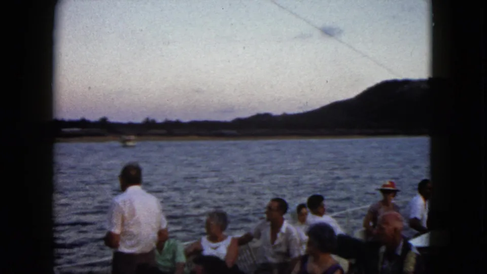 Passengers on an Acapulco boat ride in 1962 sit near the rail as the water, shoreline, and dark hills fill the background.