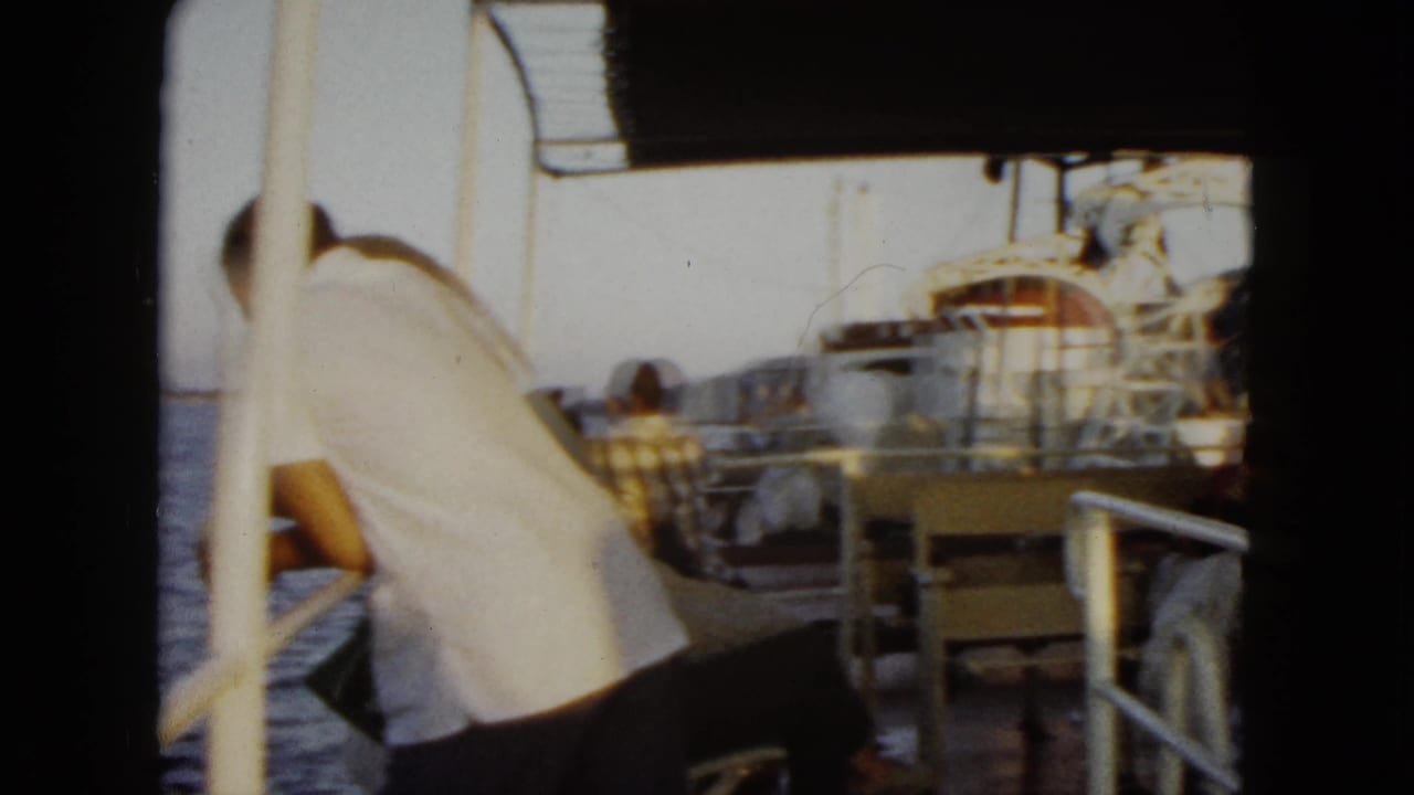 Passenger in a white shirt leans near the rail while other people sit farther along the boat deck.