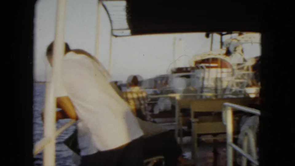 1962 Acapulco boat-deck view with a man leaning by the rail, seated passengers, sea, and coastal hills in the background.