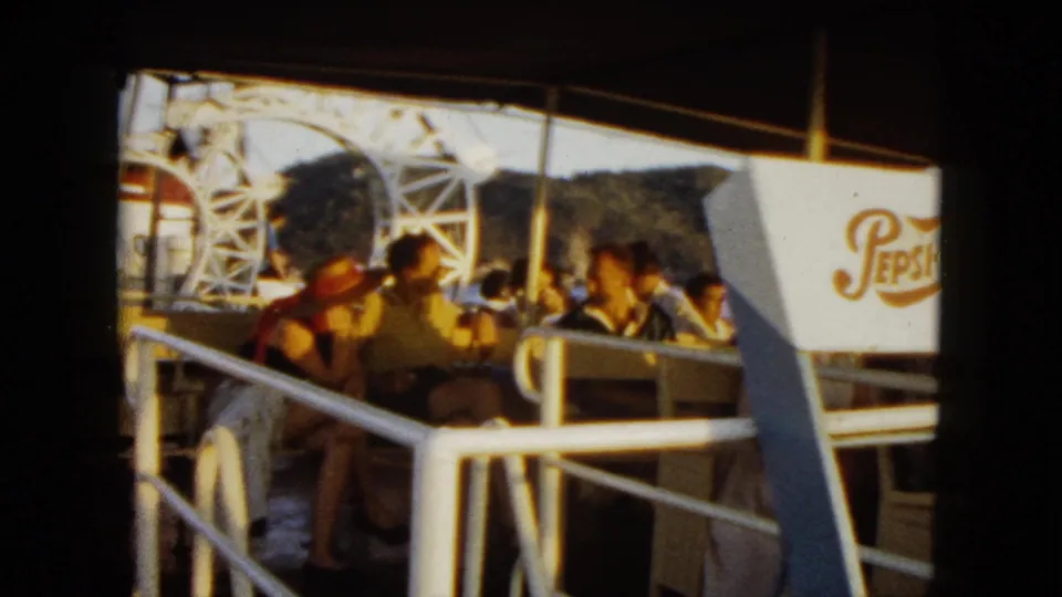 1962 Acapulco cruise frame with seated passengers on deck, white railings, canopy shade, mountains, and a Pepsi-Cola sign.